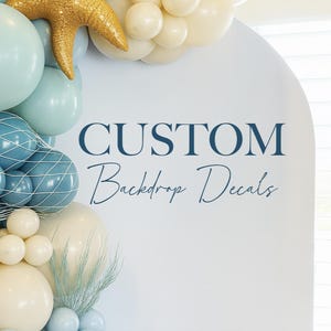 Op de afbeelding: Een witte achtergrond met de marineblauwe tekst "CUSTOM Backdrop Decals". De achtergrond is versierd met een ballonnenboog in tinten blauw, crème en goud, inclusief een gouden zeester.