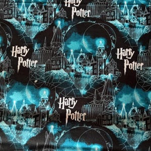 Op de afbeelding: Zwarte stof met een herhalend patroon van een witte omtrek van Zweinstein, een maan en de woorden "Harry Potter" in wit.