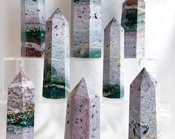 May include: A collection of eight green, grey, and pink striped crystal points arranged on a tiered acrylic display stand.