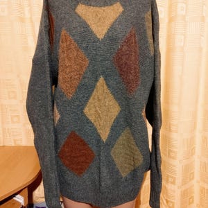 May include: A gray sweater with a crew neck and long sleeves. The sweater features a diamond pattern in shades of brown and tan. The sweater is displayed on a mannequin.