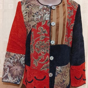May include: A long-sleeved jacket featuring a patchwork design of red, black, and tan fabric panels. The garment includes floral tapestry patterns, solid textured sections, and vertical stripes. It has a round neckline and five round buttons.