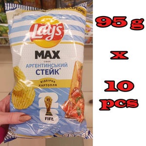 Könnte beinhalten: Eine 95-g-Tüte Lay's Max Kartoffelchips mit argentinischem Steak-Geschmack. Die Verpackung ist hellblau und weiß mit einem gelben Banner, dem Lay's-Logo, einer FIFA-Weltmeisterschaftspokal-Grafik und einem Bild von Steak mit Kräutern.