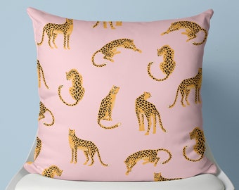 Könnte beinhalten: Ein rosa Kissen mit einem sich wiederholenden Muster aus braunen und gelben Leoparden. Das Kissen liegt auf einem weißen Stuhl mit Holzbeinen.