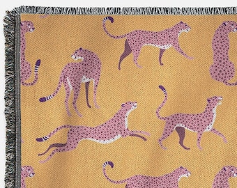 Op de afbeelding: Een geweven deken met een mosterdgele achtergrond en een herhalend patroon van roze cheeta's.