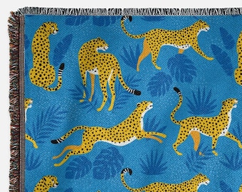 Op de afbeelding: Een geweven deken met een blauwe achtergrond en een herhalend patroon van gele cheeta's en blauwe bladeren.