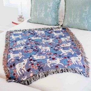 May include: A blue throw blanket with a white deer and floral pattern. The blanket has fringe on all sides.