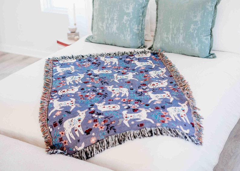 May include: A blue throw blanket with a white deer and floral pattern. The blanket has fringe on all sides.