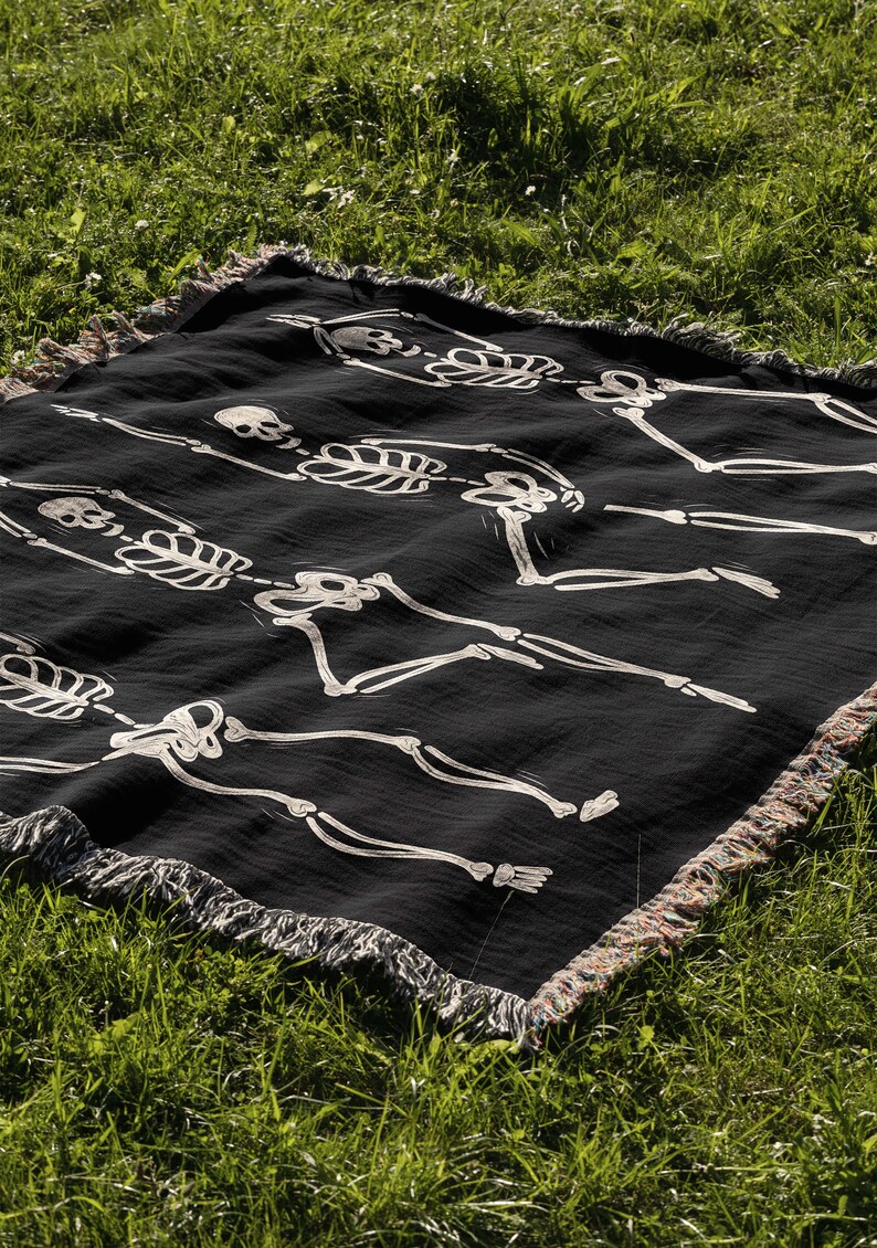 May include: Black throw blanket with a white skeleton pattern. The skeletons are dancing and have skulls. The blanket has a fringe border.