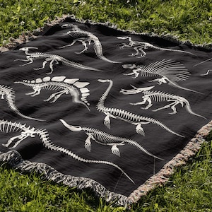 May include: Black throw blanket with a white dinosaur skeleton pattern. The blanket has a fringe border.