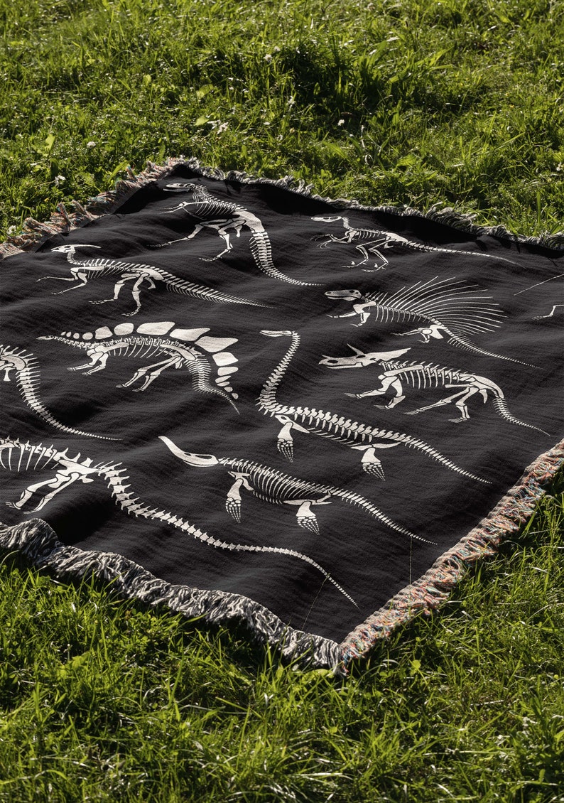 May include: Black throw blanket with a white dinosaur skeleton pattern. The blanket has a fringe border.