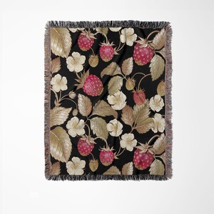 May include: A black throw blanket with a repeating pattern of strawberries, leaves, and white flowers. The strawberries are red with small seeds, and the leaves are a mix of gold and brown. The blanket has a fringed edge.