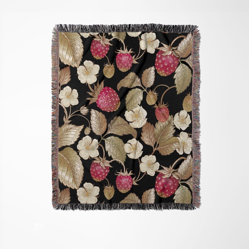 May include: A black throw blanket with a repeating pattern of strawberries, leaves, and white flowers. The strawberries are red with small seeds, and the leaves are a mix of gold and brown. The blanket has a fringed edge.