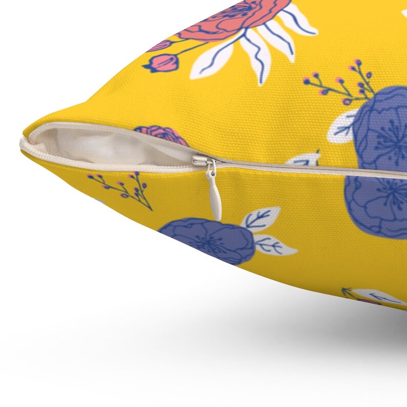 May include: A yellow pillow with a floral pattern. The pillow has a zipper closure and features pink, blue, and white flowers.