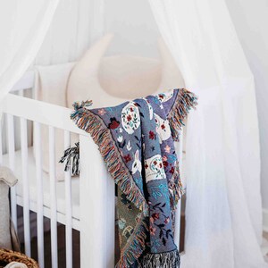 May include: A white crib with a white canopy and a colorful woven blanket hanging over the side. The blanket has a floral and animal design.