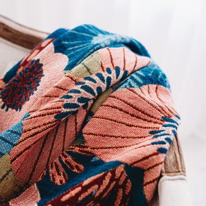 May include: A colorful throw blanket with a floral pattern in shades of blue, pink, green, and red. The blanket is draped over a chair.