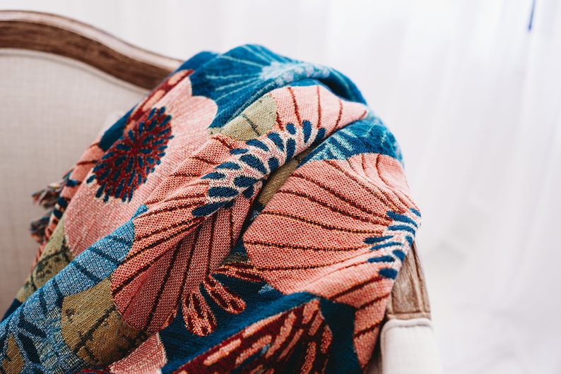 May include: A colorful throw blanket with a floral pattern in shades of blue, pink, green, and red. The blanket is draped over a chair.