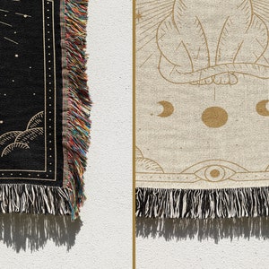 May include: A woven tapestry with a black background and gold design. The design features a cat sitting with its back to the viewer, surrounded by stars, moons, and clouds. The tapestry has fringe on all sides.