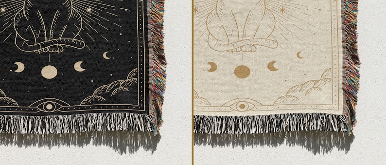 May include: A woven tapestry with a black background and gold design. The design features a cat sitting with its back to the viewer, surrounded by stars, moons, and clouds. The tapestry has fringe on all sides.