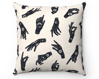 May include: A white throw pillow with a black and white pattern of hands with celestial designs. The hands are stylized and have moons, stars, and suns on them.