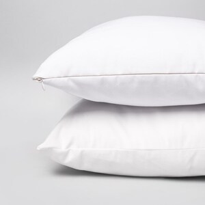May include: Two white pillowcases with a zipper closure. The pillowcases are stacked on top of each other.