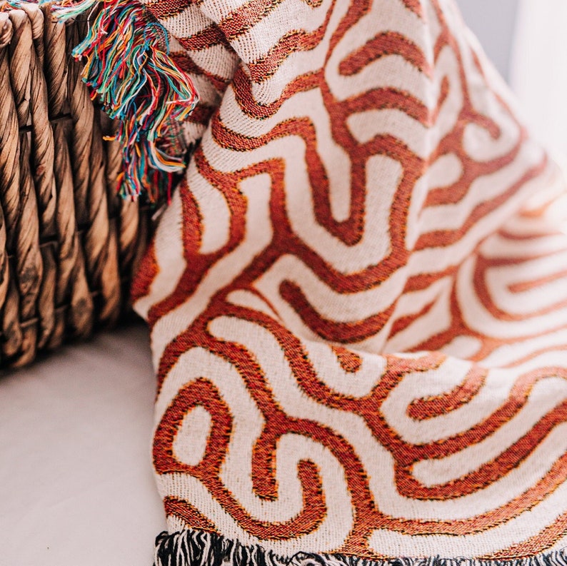 Peut inclure: Une couverture en tissu tiss&eacute; avec un motif g&eacute;om&eacute;trique dans les tons orange et blanc. La couverture a des franges sur les bords.