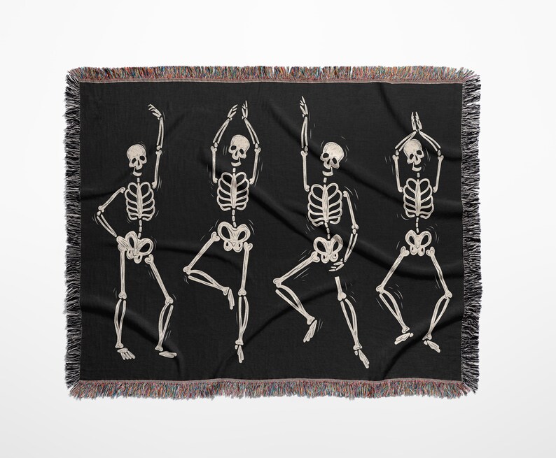 May include: A black woven throw blanket with a design of four white skeletons dancing. The skeletons are in various poses with their arms raised.