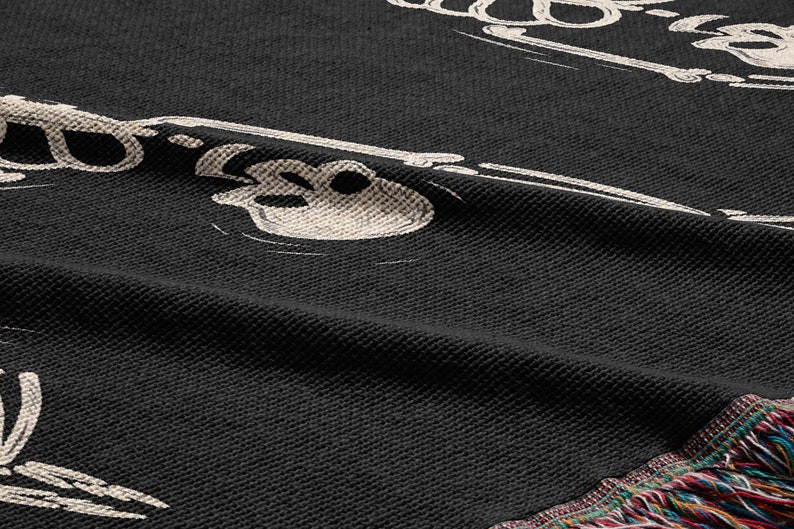 May include: Black woven throw blanket with a white skeleton design. The blanket has a fringe border.