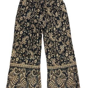 May include: Black palazzo trousers with a paisley pattern in beige and gold. The trousers have an elasticated waistband and a decorative border at the hem. The fabric appears to be lightweight and flowing.