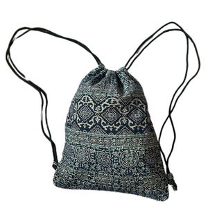 May include: A navy blue drawstring backpack with a cream geometric pattern. It features black drawstrings for closure and carrying. The fabric appears to be a soft, woven material. The bag is designed to be lightweight and easy to carry.