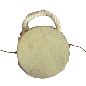 May include: A small, round, white leather drum with a white rope handle and two brown tassels.