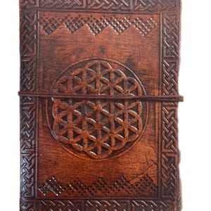 May include: A brown leather journal with a Celtic knot border and a flower of life design embossed on the front cover.