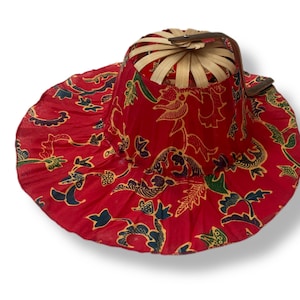 May include: A red sun hat with a wide brim and a woven crown. The hat features a floral pattern in green and gold. The brim is approximately 38 cm in diameter.