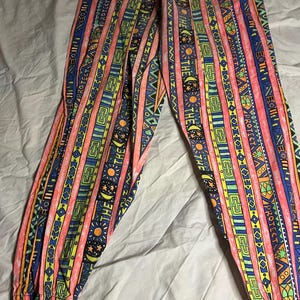 Puede incluir: Pantalones estampados de colores vibrantes. El dise&ntilde;o presenta rayas verticales en rosa, azul, amarillo y verde, con motivos geom&eacute;tricos y solares. La cintura y los pu&ntilde;os el&aacute;sticos sugieren un ajuste c&oacute;modo.