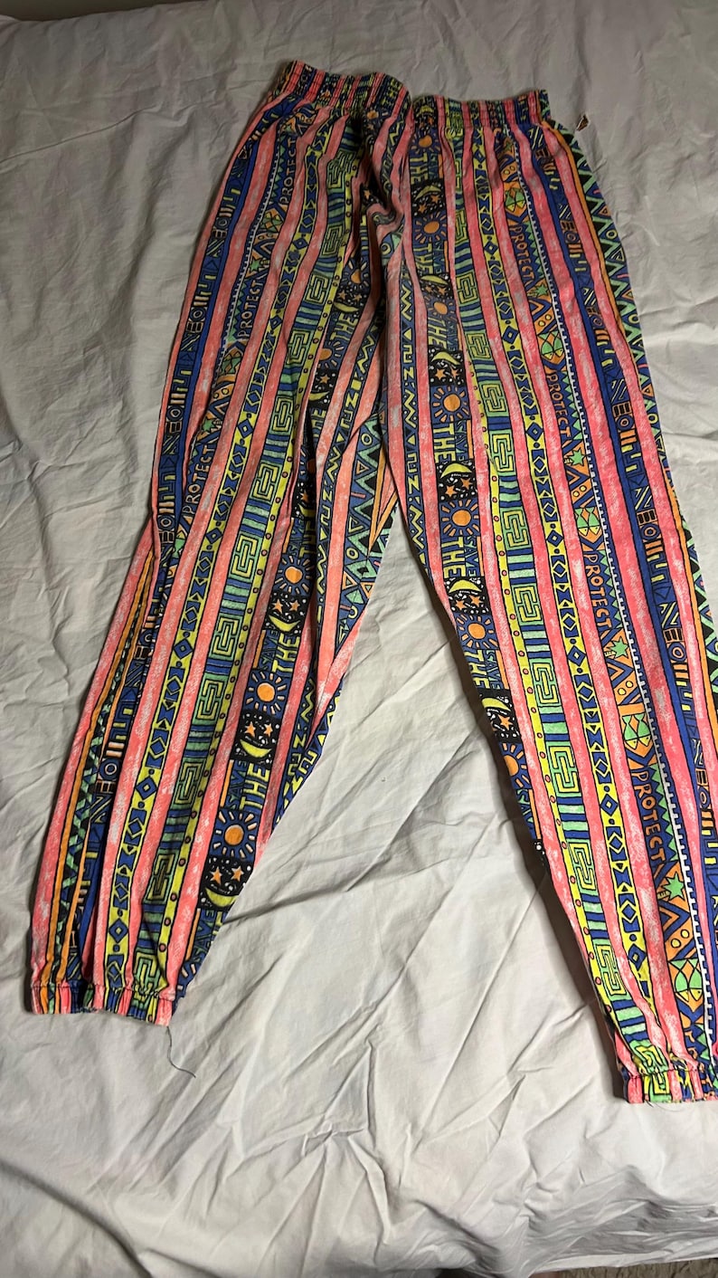 Puede incluir: Pantalones estampados de colores vibrantes. El dise&ntilde;o presenta rayas verticales en rosa, azul, amarillo y verde, con motivos geom&eacute;tricos y solares. La cintura y los pu&ntilde;os el&aacute;sticos sugieren un ajuste c&oacute;modo.