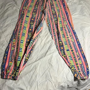 Puede incluir: Pantalones estampados con cintura con cord&oacute;n. El dise&ntilde;o presenta rayas verticales en rosa, amarillo, azul y verde, con dise&ntilde;os geom&eacute;tricos y solares. Los pu&ntilde;os el&aacute;sticos son visibles en los tobillos.