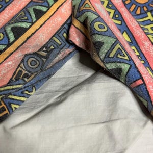 Puede incluir: Primer plano de tela colorida con un patr&oacute;n geom&eacute;trico. El dise&ntilde;o incluye rayas, tri&aacute;ngulos y motivos de sol en tonos rosa, azul, amarillo y verde. La tela parece ser parte de una prenda.