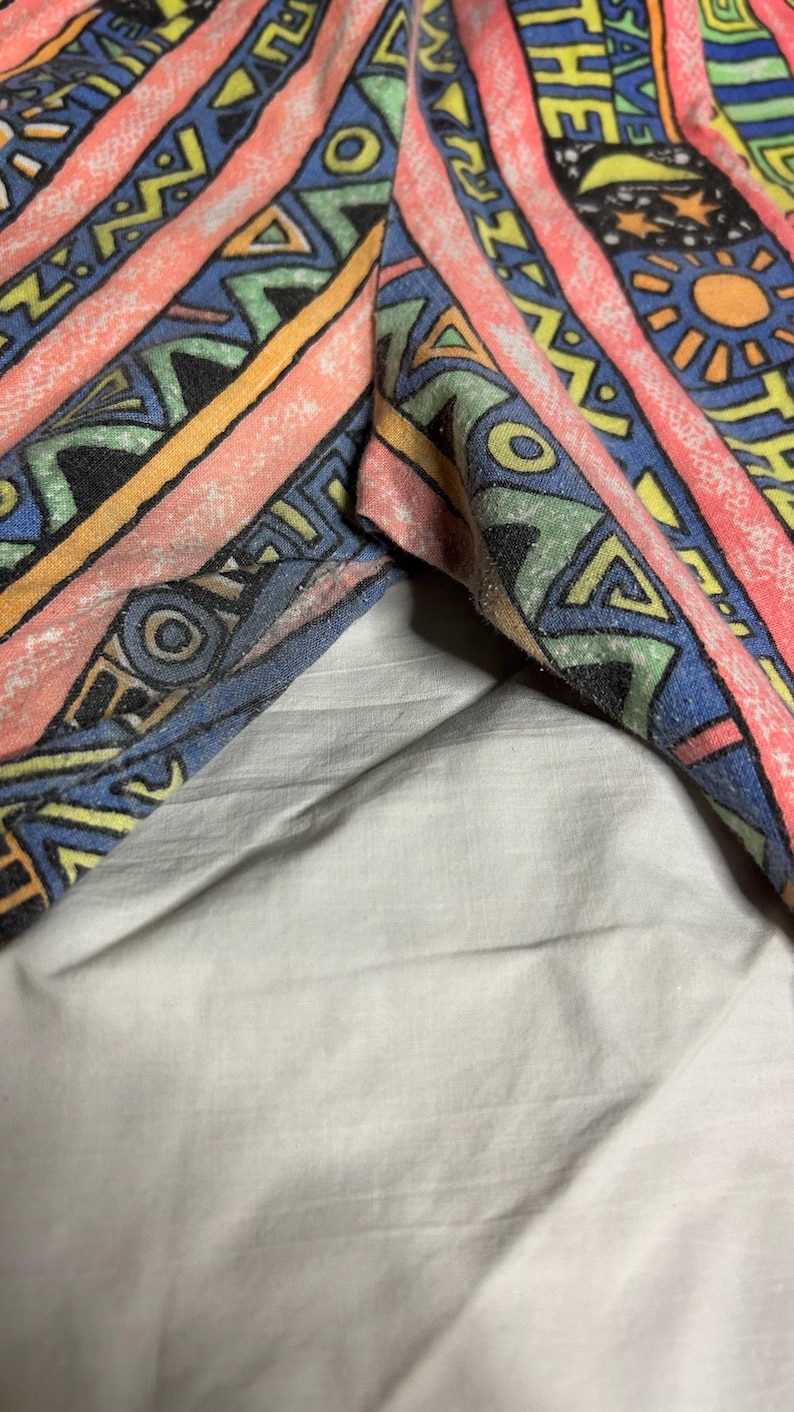 Puede incluir: Primer plano de tela colorida con un patr&oacute;n geom&eacute;trico. El dise&ntilde;o incluye rayas, tri&aacute;ngulos y motivos de sol en tonos rosa, azul, amarillo y verde. La tela parece ser parte de una prenda.