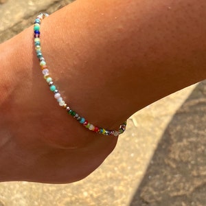 Peut inclure: Un bracelet de cheville perlé coloré avec une variété de petites perles multicolores. Le bracelet de cheville est fait d'une fine chaîne argentée.
