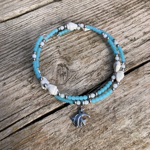 Peut inclure: Un bracelet en perles bleu et blanc avec un pendentif en forme de poisson argenté. Le bracelet est composé de petites perles rondes et a un aspect délicat et féminin.