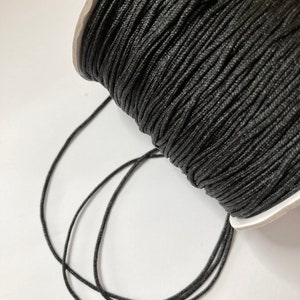 May include: A spool of black waxed cord, with a few strands of cord unraveled from the spool.