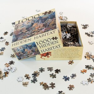 May include: A 1000 piece jigsaw puzzle box with the title "Hidden Habitat" on the front. The box is open and the puzzle pieces are scattered around it. The puzzle features an octopus and other sea creatures.