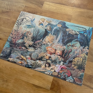 May include: A colorful jigsaw puzzle depicting an underwater scene with various sea creatures, coral, and shells. The puzzle features a variety of blues, greens, and browns, with a focus on the intricate details of the marine life.