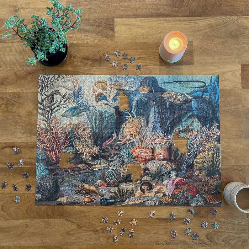 May include: A completed jigsaw puzzle depicting an underwater scene with colorful fish, coral, and sea life. The puzzle pieces are arranged on a wooden table with a lit candle and scattered puzzle pieces.