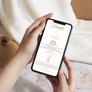May include: A smartphone displays wedding details, held by a person. The screen shows elegant script and icons for ceremony and reception information. The background is a soft, neutral tone.
