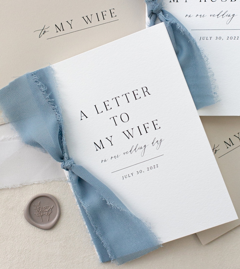 May include: A white card with the text "A Letter to My Wife on our wedding day July 30, 2022" and a blue ribbon tied around it.