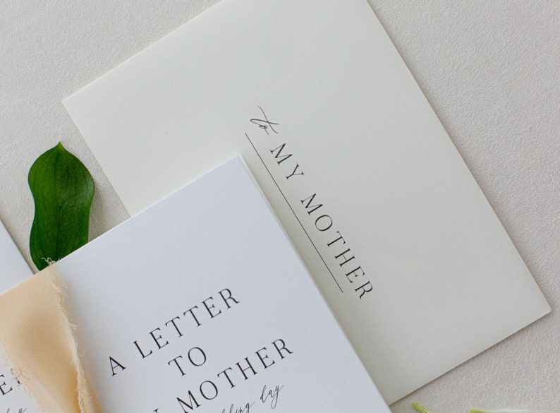 May include: A white card with the text "A Letter to My Mother" printed in black. The card is sitting on top of a cream-colored envelope with the text "to My Mother" printed in black.