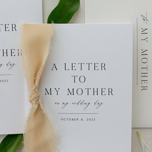 May include: Two white cards with the text "A Letter to My Father on my wedding day October 8, 2022" and "A Letter to My Mother on my wedding day October 8, 2022". A beige ribbon is tied around the cards.