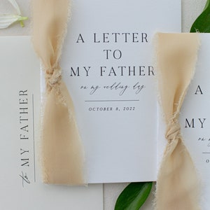 May include: A white card with black text that reads "A Letter to My Father on my wedding day October 8, 2022". The card is tied with a beige ribbon.