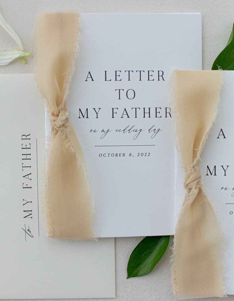 May include: A white card with black text that reads "A Letter to My Father on my wedding day October 8, 2022". The card is tied with a beige ribbon.