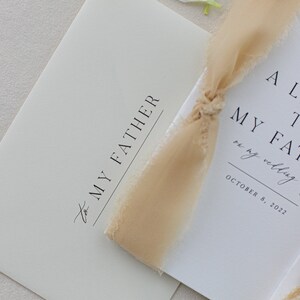 May include: A white card with the text "A Letter to My Father on my wedding day" and the date "October 8, 2022". The card is tied with a beige ribbon.